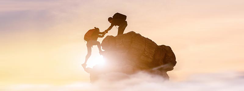 Zwei Bergsteiger, die sich bei Sonnenaufgang gegenseitig beim Aufstieg auf einen Berg helfen.