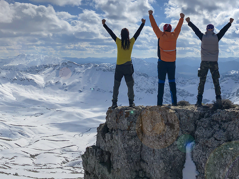 Drei Bergsteiger auf einem Berg, die die Arme nach oben strecken